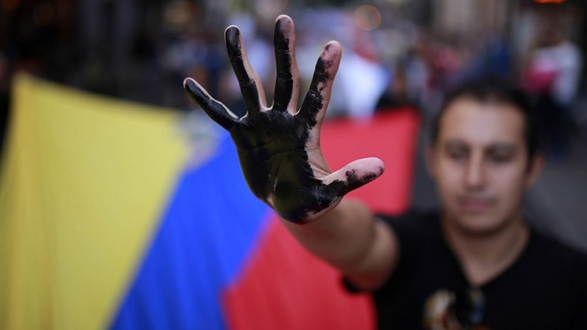 Foto: Investor's Business Daily. Un manifestante muestra su mano pintada de negro al mismo tiempo que porta una bandera de Ecuador para protestar en contra de Chevron y la contaminación por petróleo en la región amazónica de Ecuador durante una manifestación en Madrid, España, en 2013. Ecuador ganó una sentencia judicial de $19 mil millones de dólares por daños y perjuicios en 2013, pero que fue posteriormente revocada debido a actividades ilícitas por la parte del abogado estadounidense de los demandantes. (AP)