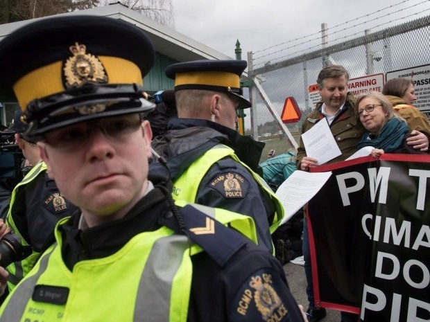 Un oficial de la Real Policía Montada lee una orden judicial a la líder del Partido Verde, Elizabeth May, derecha, y al diputado del NDP, Kennedy Stewart, segundo a la derecha, antes de ser arrestados después de unirse a los manifestantes fuera de las instalaciones del Kinder Morgan en Burnaby, Colombia Británica, el viernes 23 de marzo de 2018. Darryl Dyck / THE CANADIAN PRESS