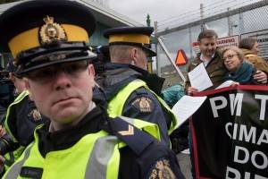 Un oficial de la Real Policía Montada lee una orden judicial a la líder del Partido Verde, Elizabeth May, derecha, y al diputado del NDP, Kennedy Stewart, segundo a la derecha, antes de ser arrestados después de unirse a los manifestantes fuera de las instalaciones del Kinder Morgan en Burnaby, Colombia Británica, el viernes 23 de marzo de 2018. Darryl Dyck / THE CANADIAN PRESS
